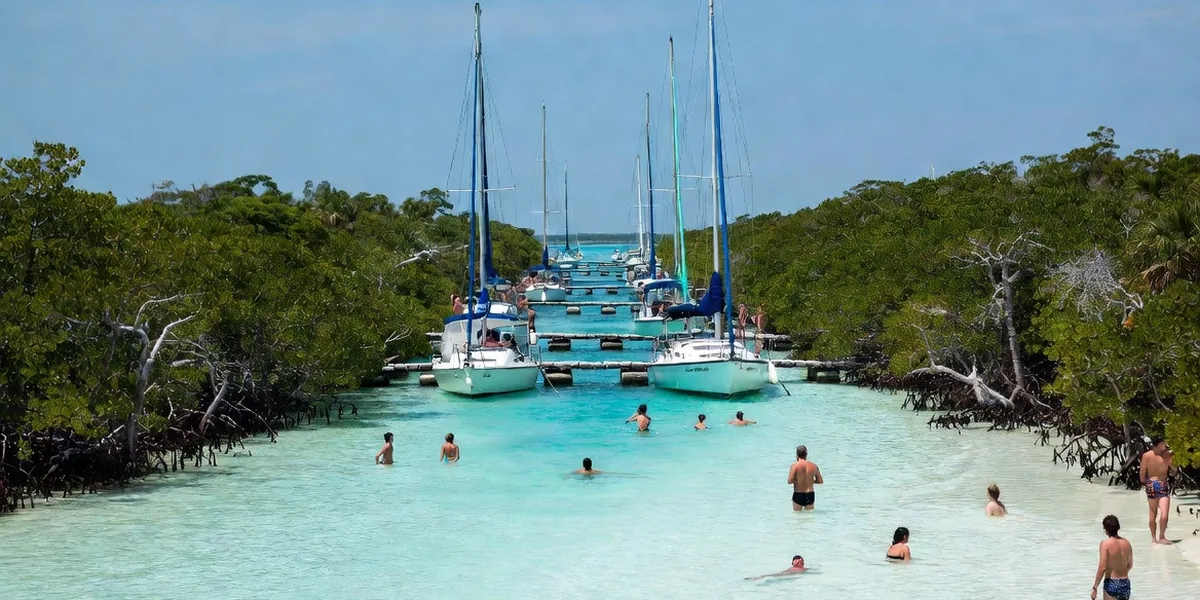 Boats gathered in the narrow Pirate Channel of Bacalar with swimmers on the white shallow banks