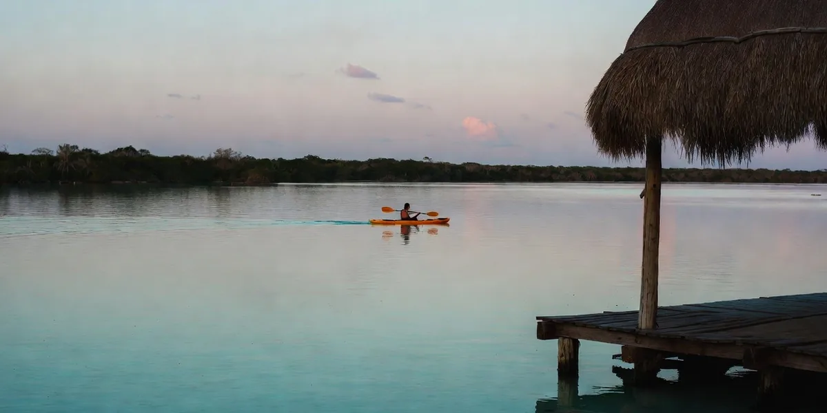 Kayaker on the flat morning water of Bacalar Lagoon near a wooden dock
