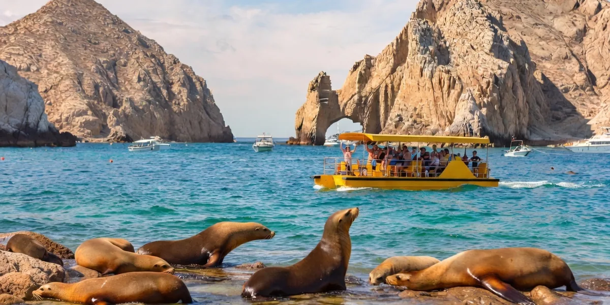 Water taxi passing the El Arco rock arch at Land's End, Cabo San Lucas, with a cruise ship anchored in the bay