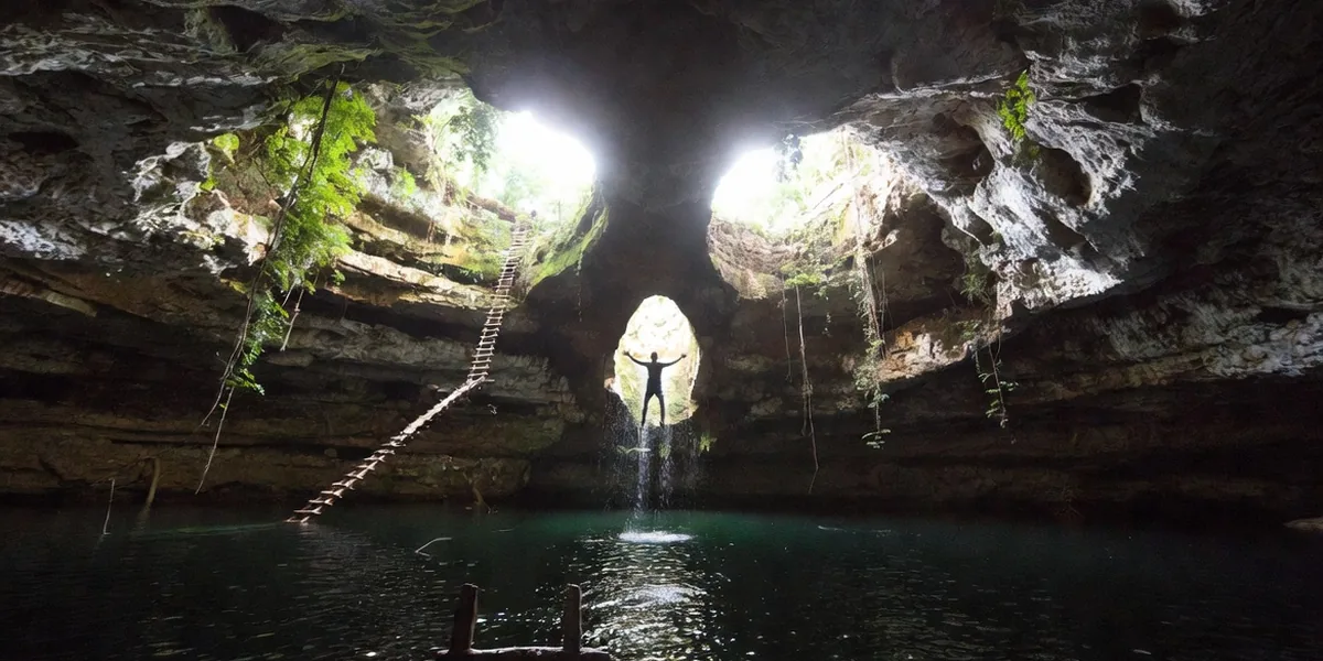 Jumper dropping through the skull-eye opening into the clear pool of Cenote Calavera near Tulum