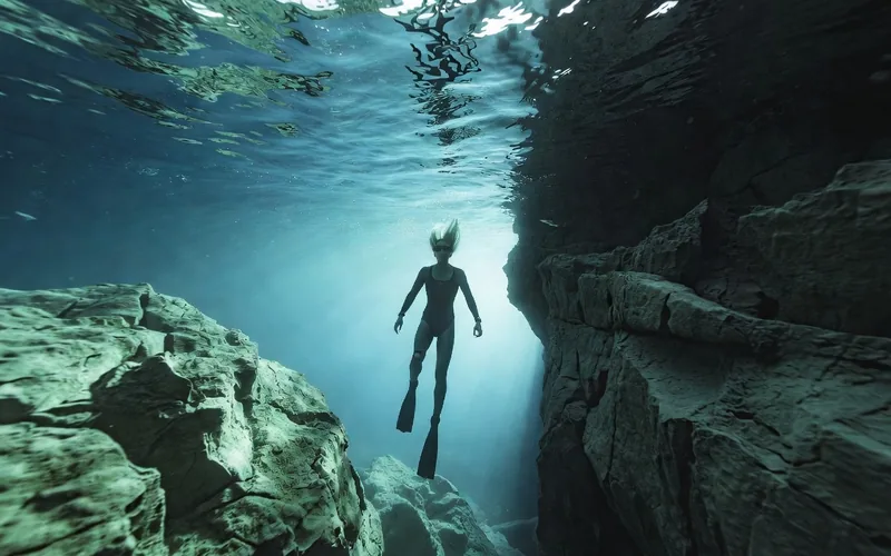 Freediver descending in the clear blue cavern water of Dos Ojos cenote