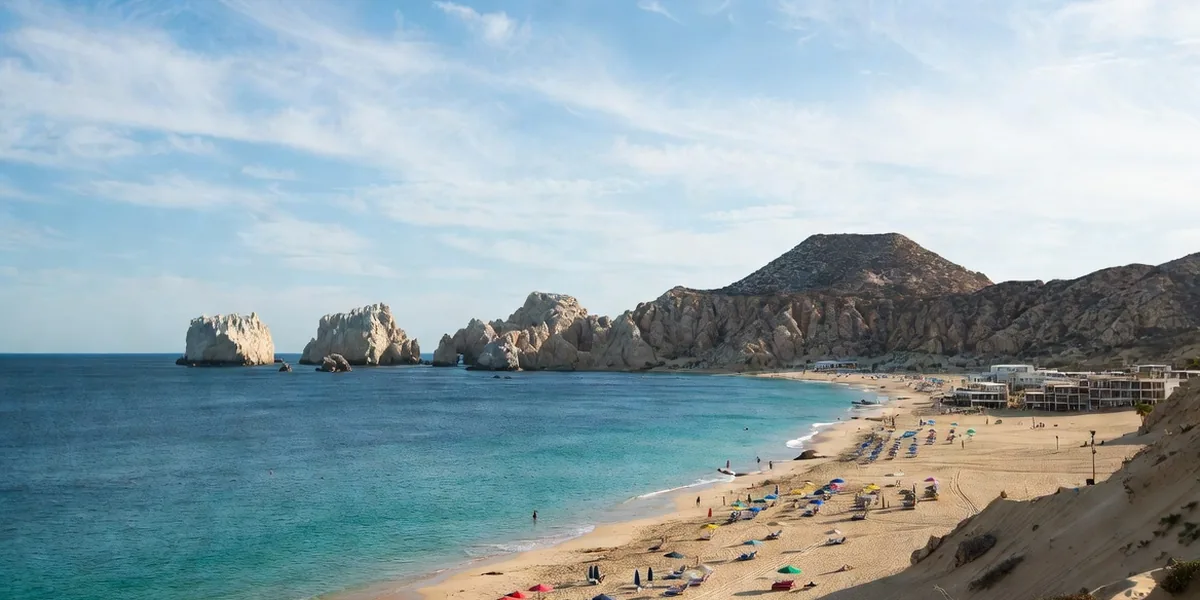 Golden sand and calm swimmable water at Médano Beach with Land's End on the horizon, Los Cabos