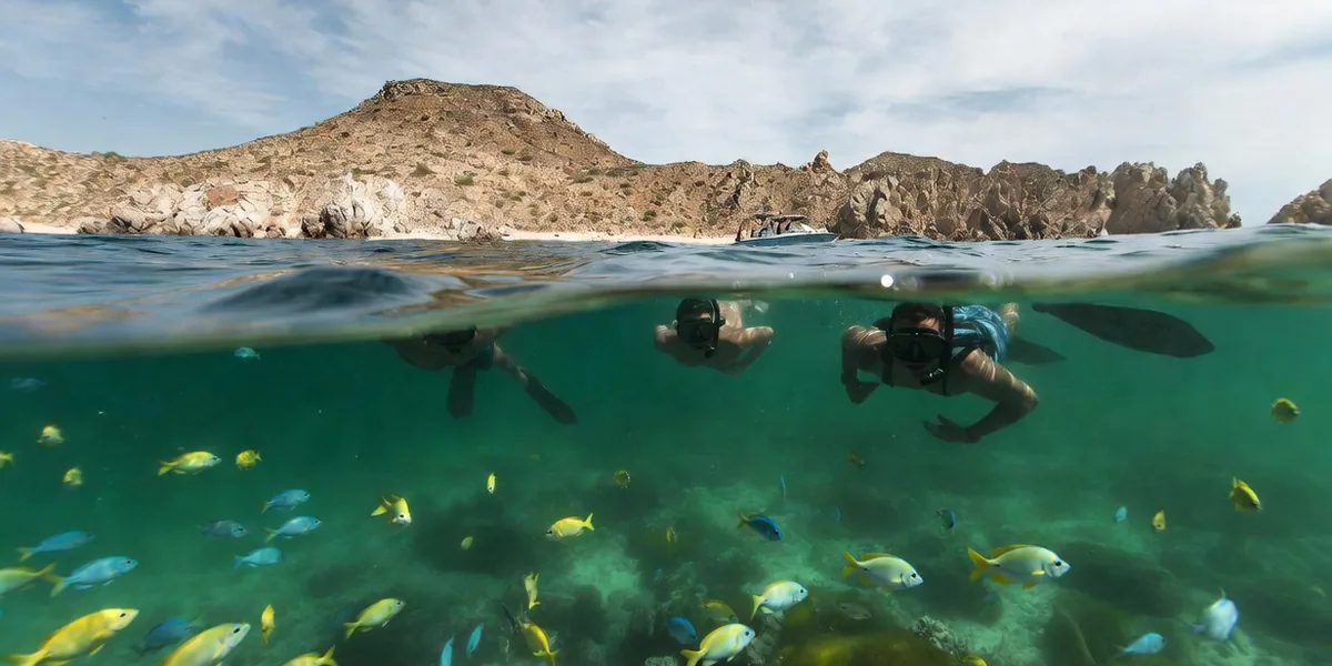 Snorkelers over rocky reef and tropical fish in the clear horseshoe cove of Santa Maria Bay, Los Cabos