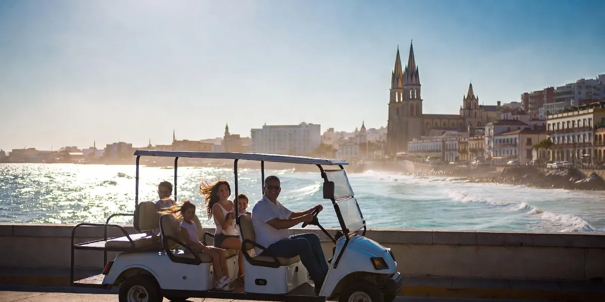 Open-air pulmonía taxi driving the Mazatlán malecón with the historic center and Pacific coastline behind
