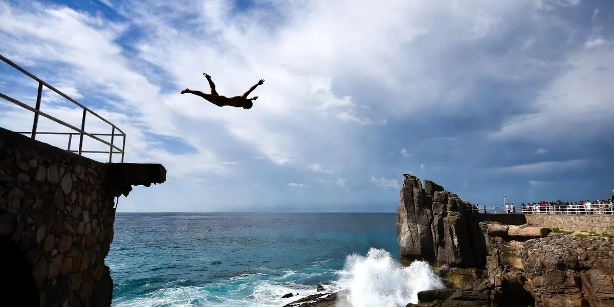 Cliff diver mid-air off the rock platform at Mazatlán's Glorieta with spectators watching