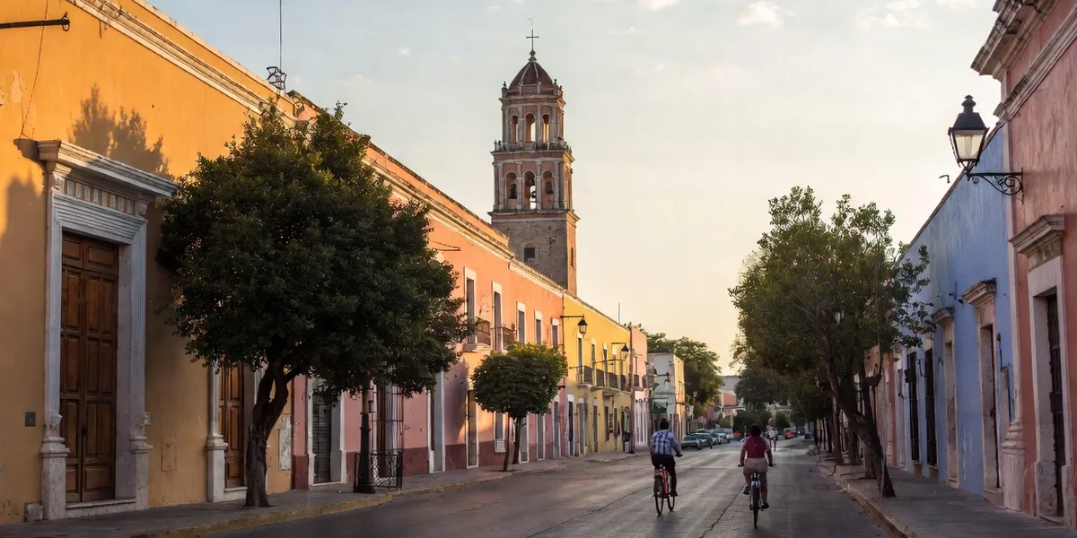 Pastel colonial facades and laurel trees on a quiet street in Mérida's historic center