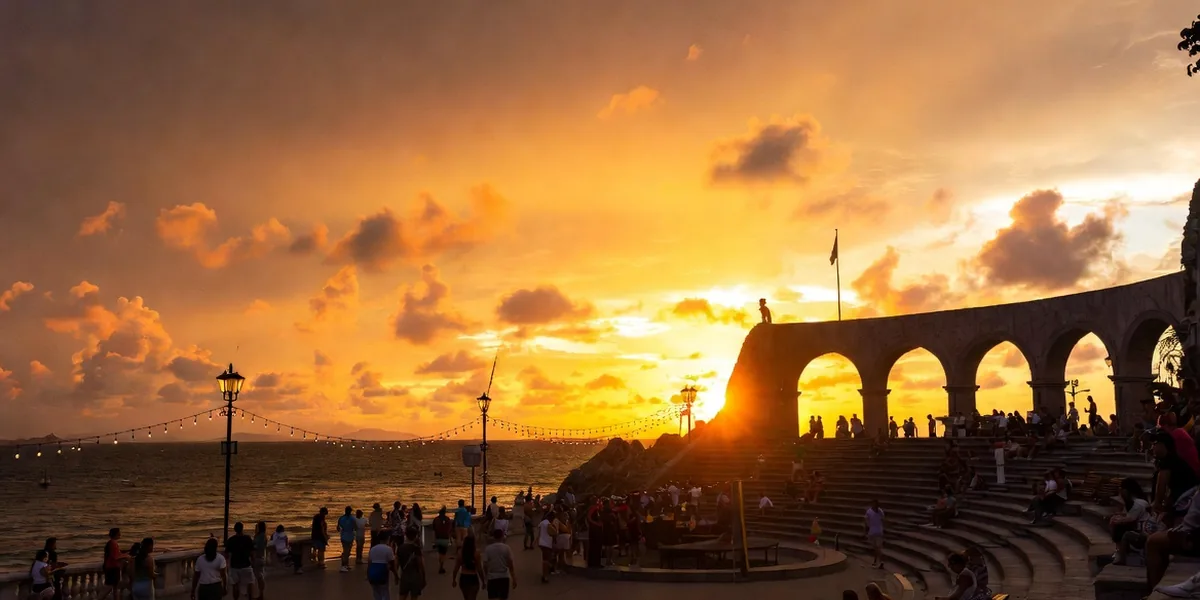 Crowds strolling the Puerto Vallarta malecón at sunset with the arches silhouetted over Banderas Bay