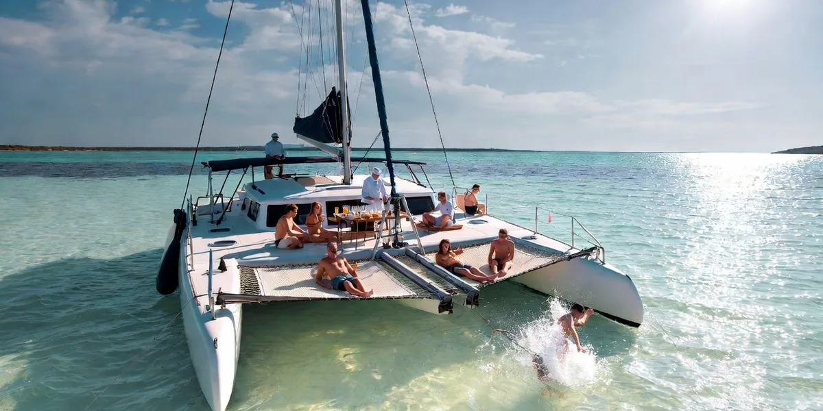 Luxury sailing catamaran anchored over pale turquoise shallows off the Riviera Maya with guests on the trampoline nets