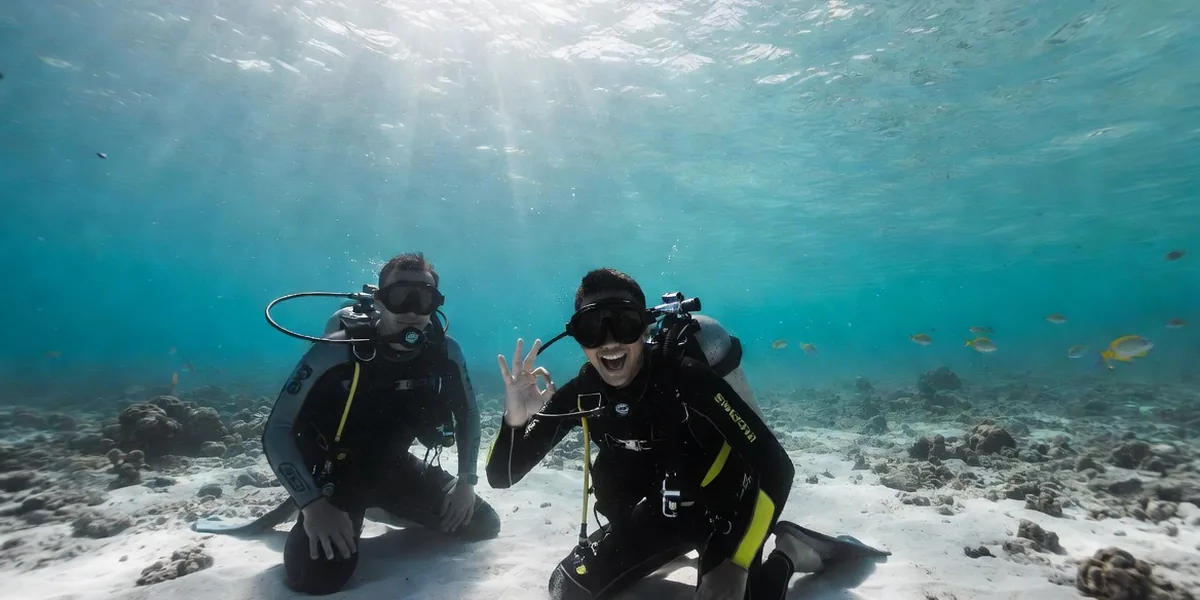 Open Water student diver kneeling on white sand in clear Caribbean shallows with an instructor during a certification dive