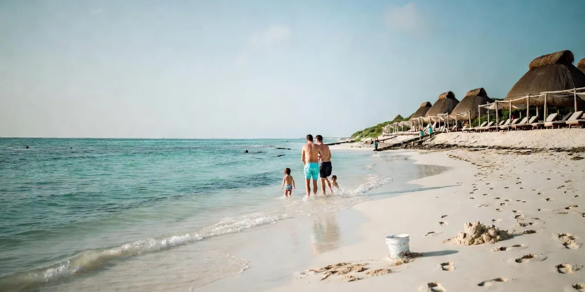 Family playing in calm shallow water in front of a kid-friendly beach hotel in Tulum