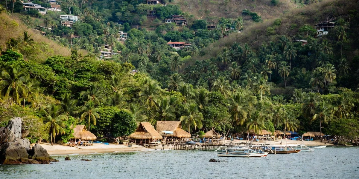 Yelapa's palm-covered cove from the water with palapas on the beach and pangas at the pier